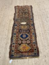 An antique hand knotted Caucasian runner rug, the brown ground with multiple guls and bordered 300cm