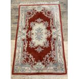 A Chinese washed wool rug, the red field with floral medallion and bordered 264cm x 151cm