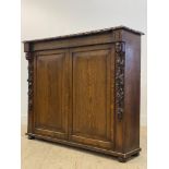 A Victorian oak side cabinet, the floral moulded top above two panelled doors enclosing shelves,