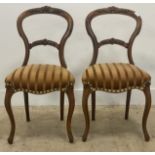 A pair of Victorian walnut balloon back dining chairs with floral carved crest over upholstered