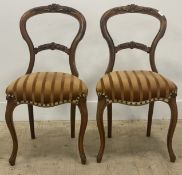A pair of Victorian walnut balloon back dining chairs with floral carved crest over upholstered