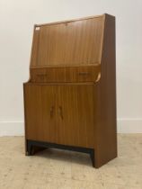 A mid century teak bureau, the fall front revealing a fitted interior, above a drawer and cupboard