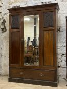 An Edwardian mahogany wardrobe, the projecting cornice above floral carved and field panels flanking