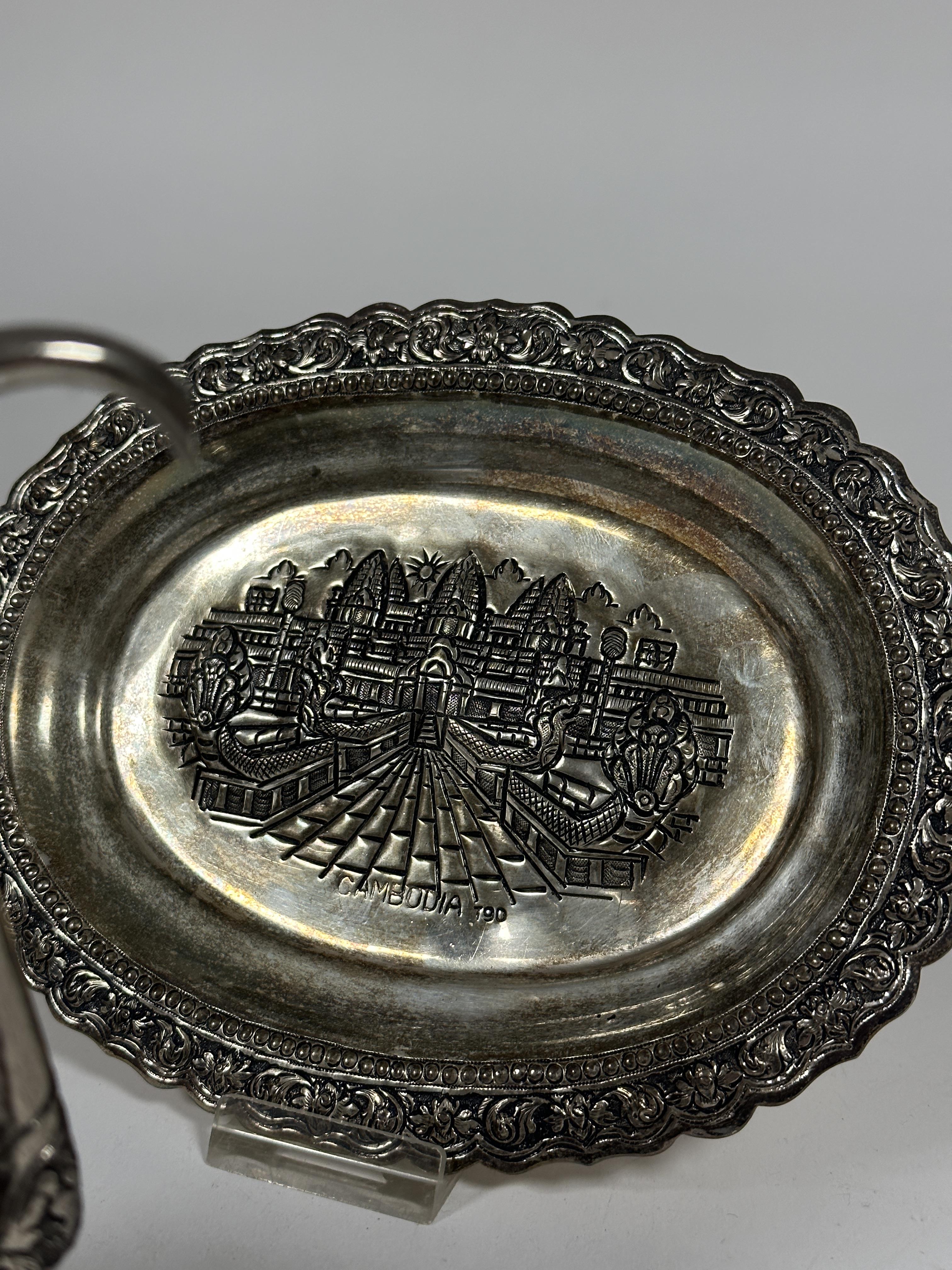 A Cambodian oval white metal chased offering dish with temple panel to centre enclosed within a - Image 2 of 2