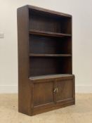 An oak open bookcase, early 20th century, fitted with two fixed shelves over two panelled cupboard