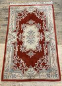 A Chinese washed wool rug, the red field with floral medallion and bordered 264cm x 151cm