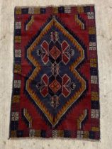 A hand knotted Baluchi rug, the red field with medallion and bordered 137cm x 88cm