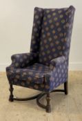 A high back wing chair of 18th century design, upholstered and with squab seat, raised on turned and