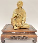 A Chinese ceramic/plaster figure of a seated man with a basket of mangoes (h- 20cm), on a carved har