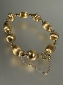 A yellow metal circular and oval bead chain link bracelet, each bead with textured finish, with ring