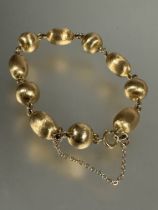 A yellow metal circular and oval bead chain link bracelet, each bead with textured finish, with ring