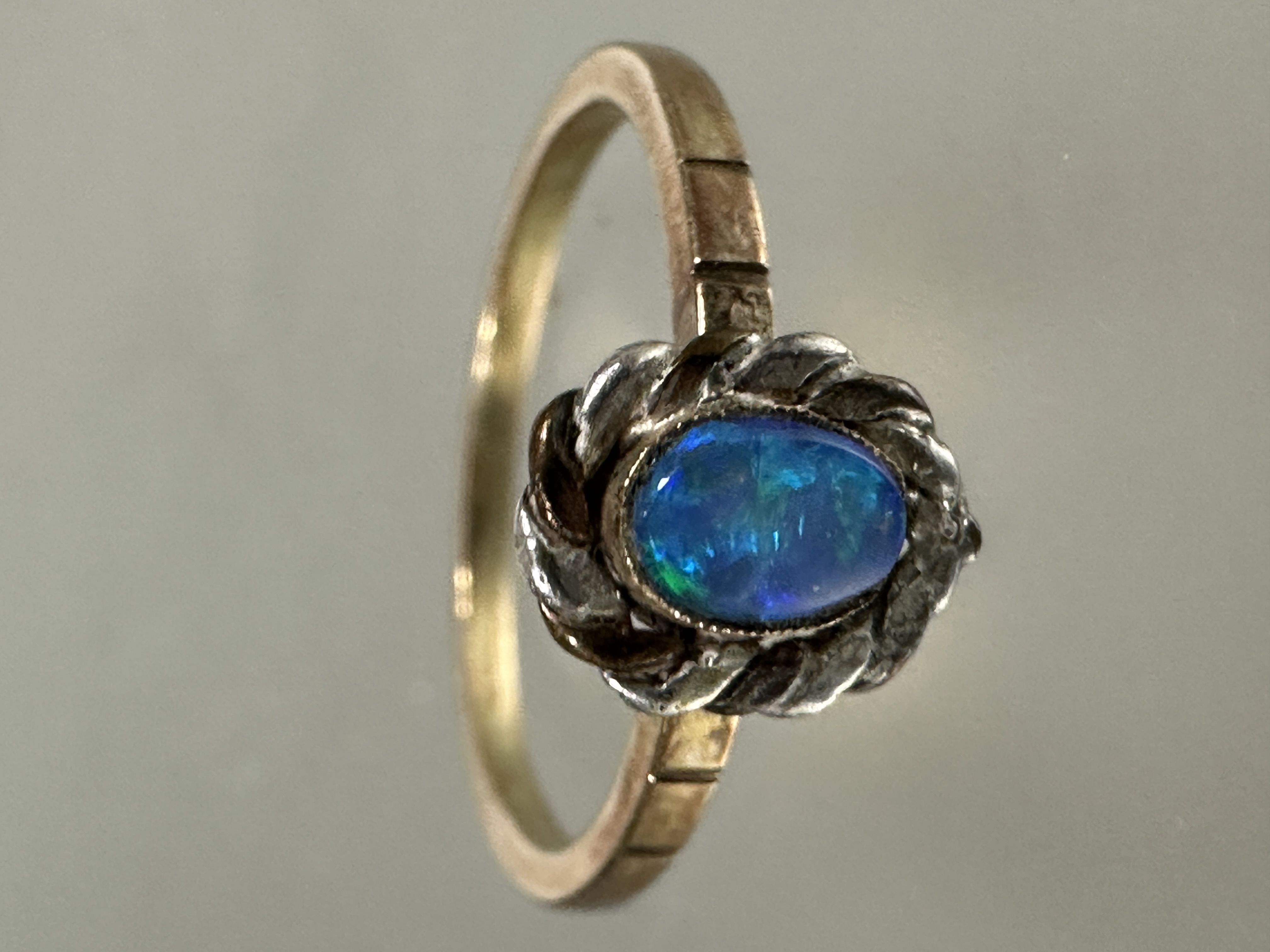 A yellow and white metal artisan made ring, set oval black opal enclosed in rub over setting and