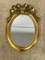 A gilt framed wall mirror of oval outline surmounted by bow ribbon moulded pediment 60cm x 43cm.