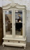 A French style cream painted armoire, the two mirrored doors enclosing an interior with slides and