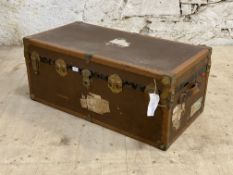 An early 20th century leather and brass bound streamer trunk with old paper labels to exterior.