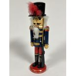 An Austrian traditional wooden soldier nutcracker figure with peaked hat raised on circular base, (H