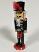 An Austrian traditional wooden soldier nutcracker figure with peaked hat raised on circular base, (H