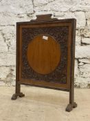 An early 20th century carved oak and walnut fire screen, the panel decorated with floral motifs.