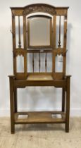 An Arts and Crafts period oak hall stand, the carved back with mirror to centre and six coat