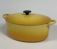 A Le Creuset oval cast iron casserole dish and cover with gradated yellow enamel finish, shows no