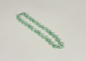 A Chinese jadeite single strand bead necklace, the uniform spherical celadon beads spaced by smaller