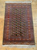 A hand knotted Bokhara rug, the green field decorated with three rows of guls