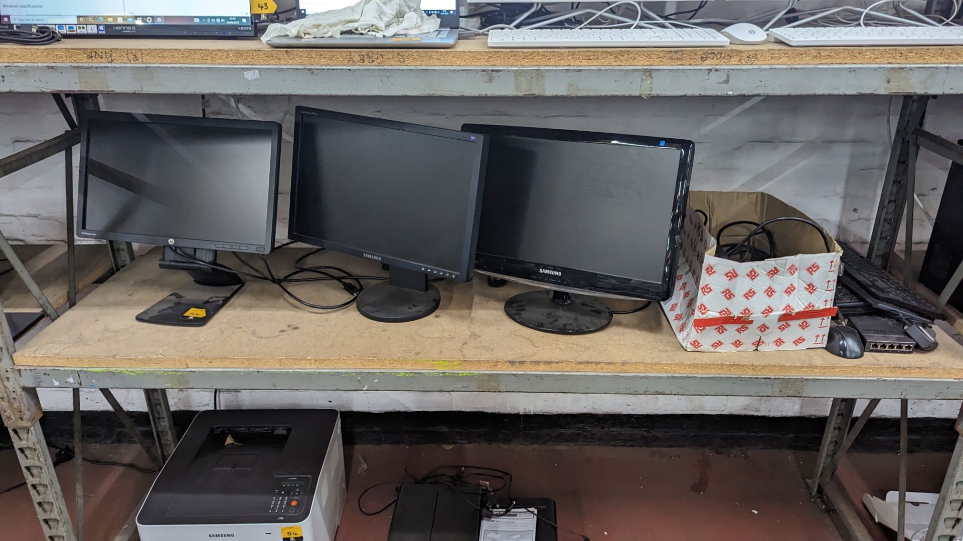 The contents of a shelf of assorted IT equipment including monitors, cables, keyboards, headphones &