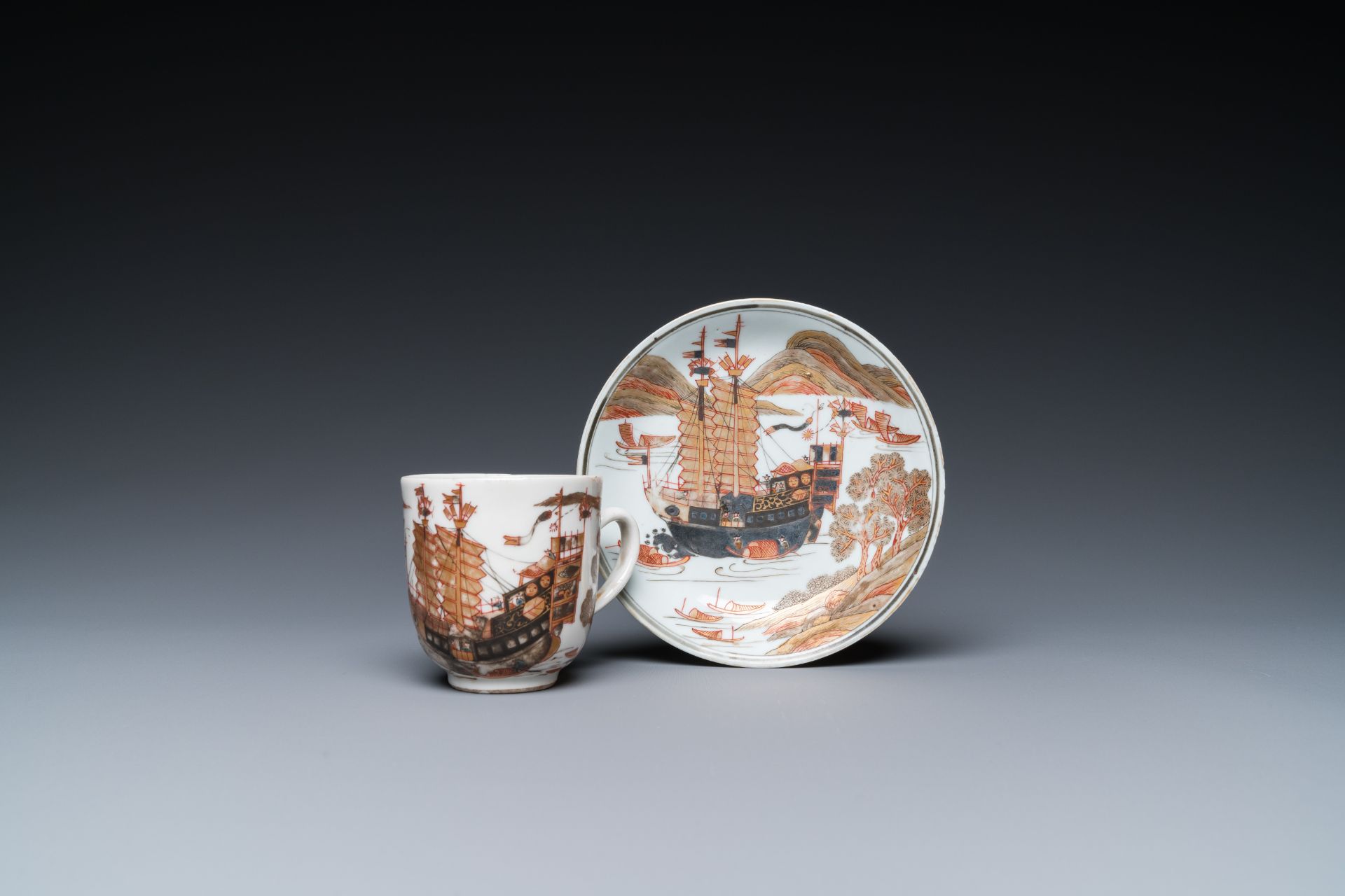 A rare Chinese gilt, grisaille and iron-red cup and saucer with a merchant vessel, Yongzheng/Qianlon