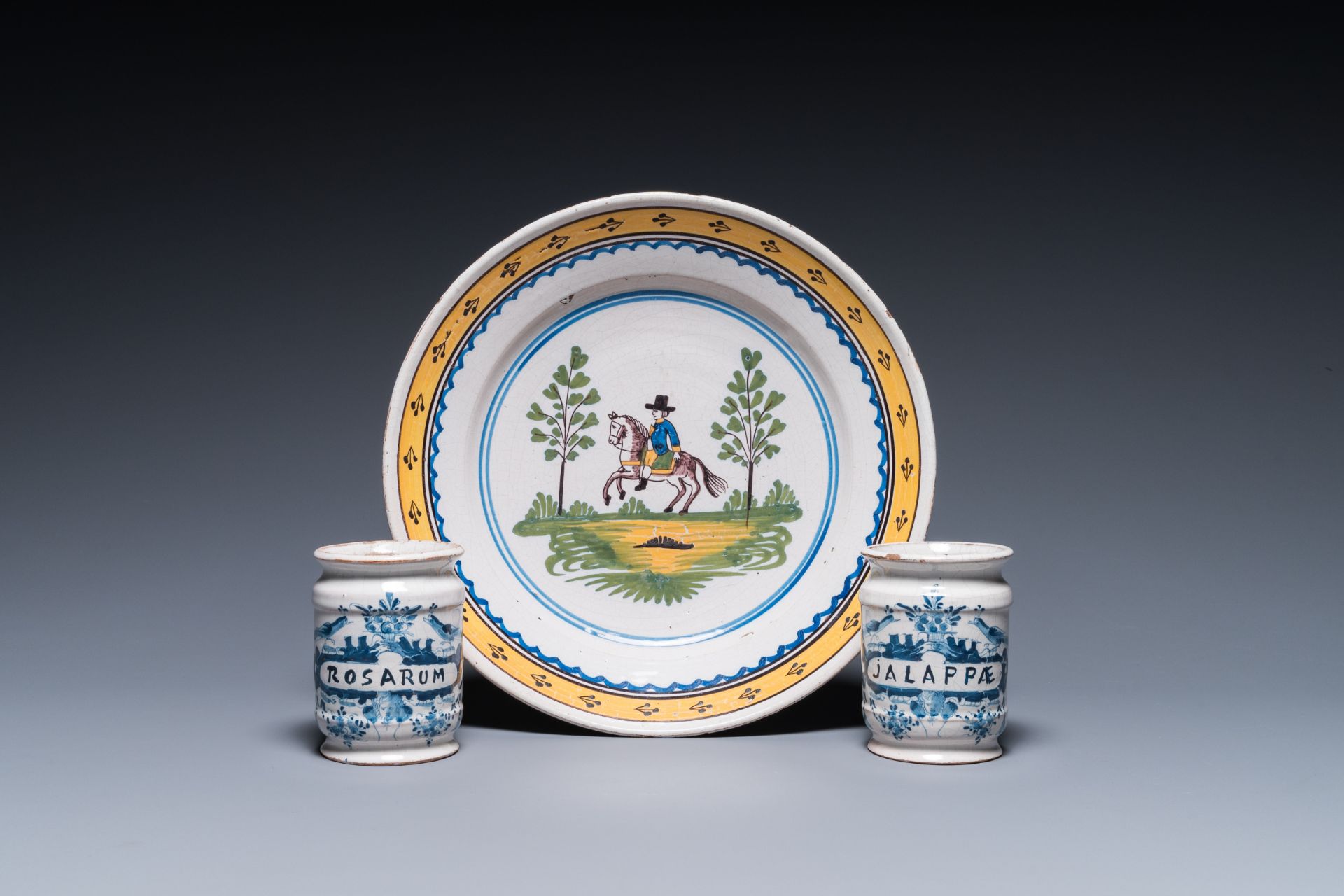 Two Dutch Delft blue and white drug jars and a polychrome Brussels faience dish with a rider on hors