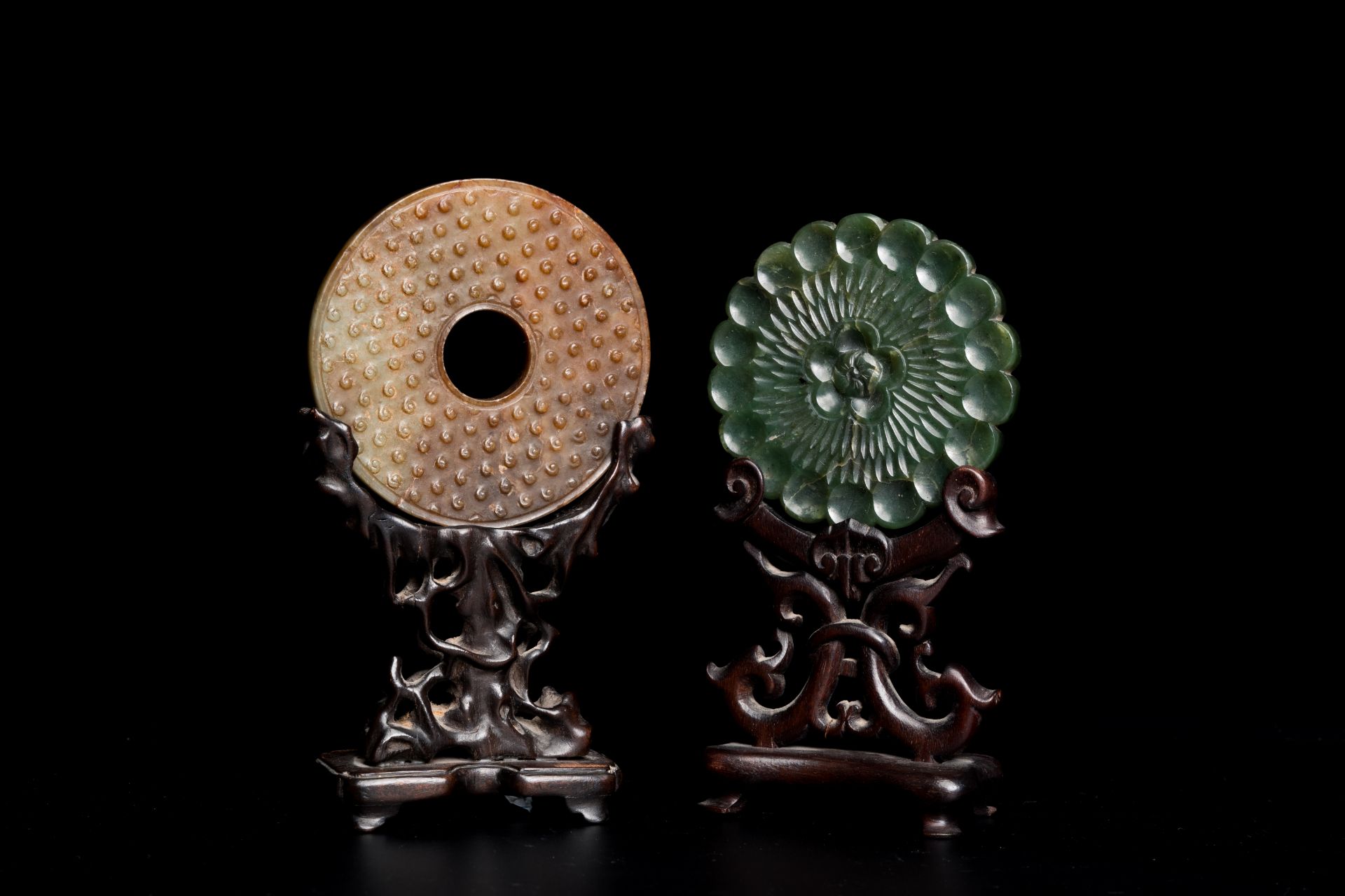 A Chinese celadon and russet jade 'bi' disc and a spinach green flower-shaped pendant on wooden stan