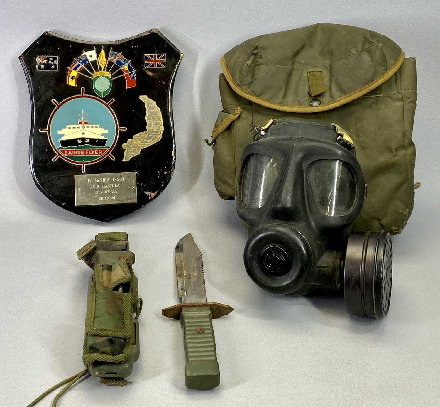 A GAS MASK IN CLOTH BAG, a sheath knife with 19cms blade and a wall plaque, Saigon Flyer, D McNiff