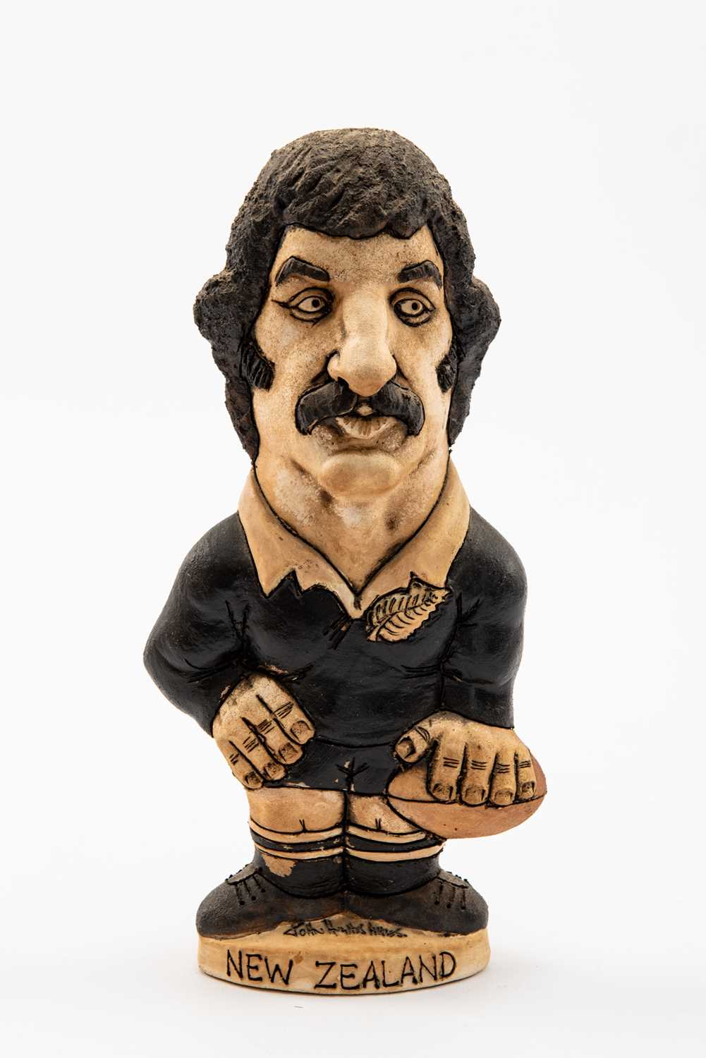 GROGG CARICATURE BY JOHN HUGHES OF GRAHAM MOURIE standing on titled base, wearing his All Blacks