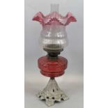 AN IRON BASED OIL LAMP - fine Cranberry glass reservoir and shade, 57cms total