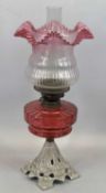 AN IRON BASED OIL LAMP - fine Cranberry glass reservoir and shade, 57cms total