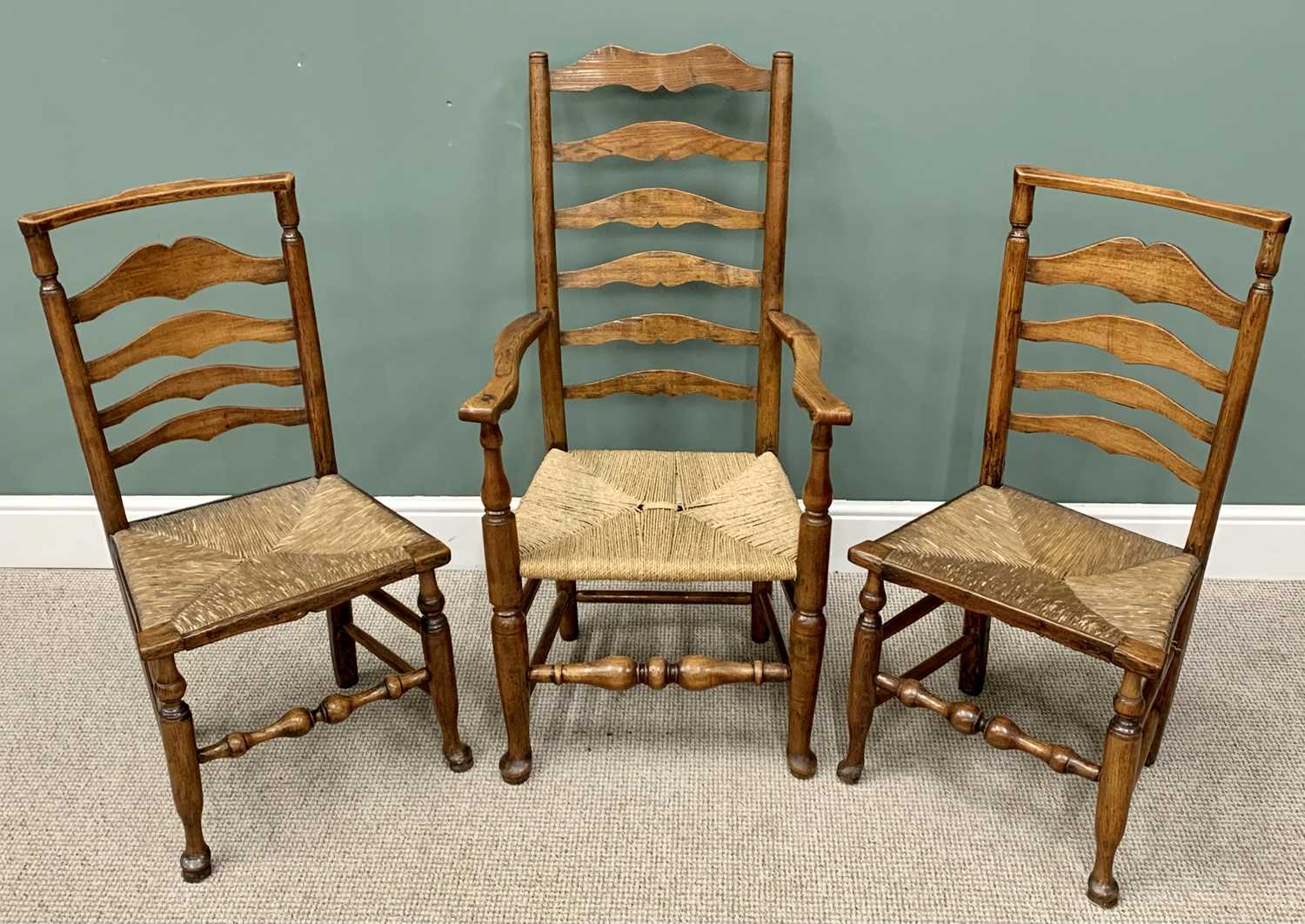 THREE RUSH SEATED LADDERBACK CHAIRS including one carver, on hoof supports, 114cms H, 60cms W, 43cms