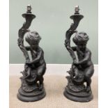 PAIR OF COMPOSITION CHERUBIC BLACK LAMPS, the figures seated holding leaf form fitting mounts on