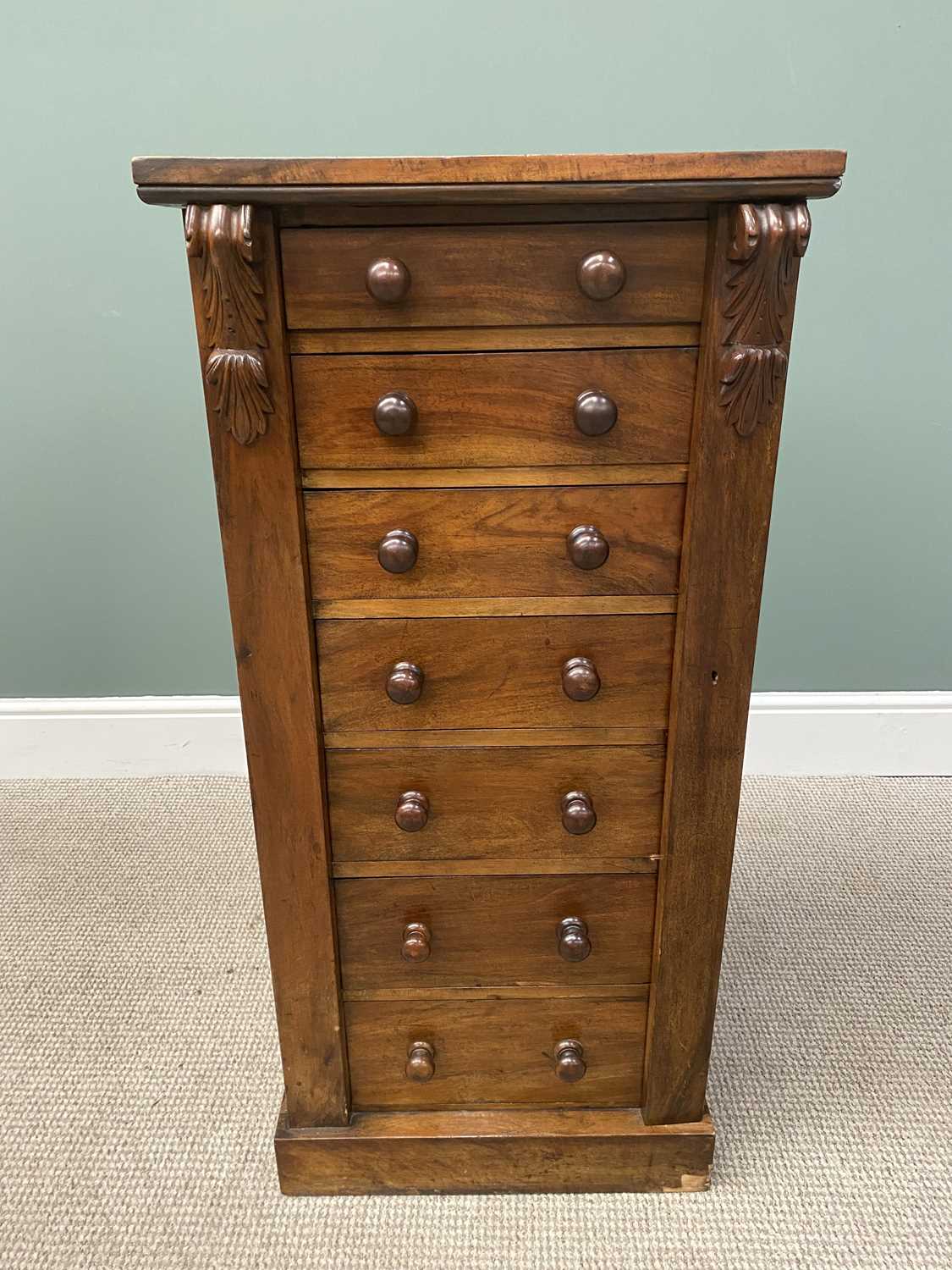 VICTORIAN MAHOGANY WELLINGTON CHEST OF SEVEN OPENING DRAWERS, with carved corbel upper detail on a