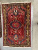 IRANIAN WOOLLEN RUG, red ground with repeating central block motif and multi-coloured triple