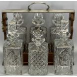 20TH CENTURY SILVER PLATED & MAHOGANY THREE-BOTTLE TANTALUS & THREE FURTHER CUT GLASS DECANTERS, the