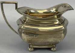 SILVER MILK JUG BY WALKER & HALL, having a gadrooned upper edge with angular handle, on four ball