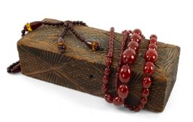 ASSORTED CHERRY AMBER COLOURED BEADS, three strings of various sizes, in carved wooden rectangular