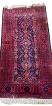 PERSIAN HANDMADE WOOLEN RUG, red and blue ground with tasselled ends, traditional pattern central