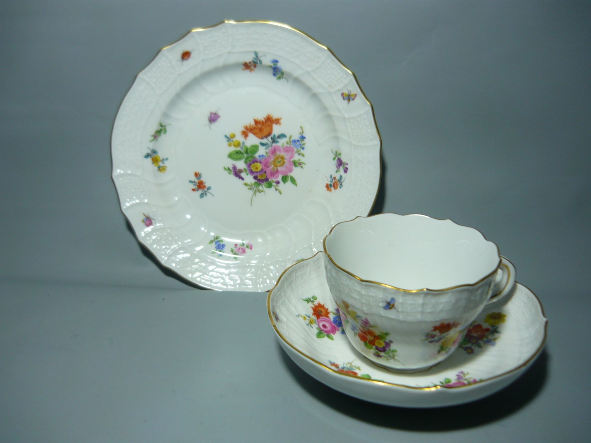 Meissen (Schwerter). Kaffeetasse mit Untertasse samt Kuchenteller. Reiche Malerei mit Blumen