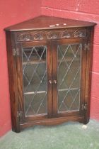 An oak Jaycee floor standing corner cupboard, canted front, demi-lune carving to frieze, two lead