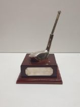 White metal golfing trophy having propelling pencil and raised on wooded mount. Shipping Group (A).