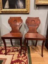 Late 19th/ Early 20th century A pair of mahogany hall chairs With carved detail to the backs