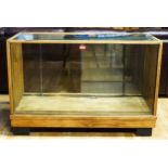 A 1930's light oak shop display unit with one glass shelf, sliding doors, 136 x 59 x 92cm.