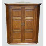 An Arts & Crafts style oak wall hanging corner cabinet by 'Thistleman' of Leven, the moulded cornice