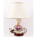 A Moorcroft magnolia pattern table lamp, decorated against an ivory ground, with cream shade.