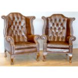 A pair of Georgian style wingback armchairs, upholstered in tan leather with buttoned backs,